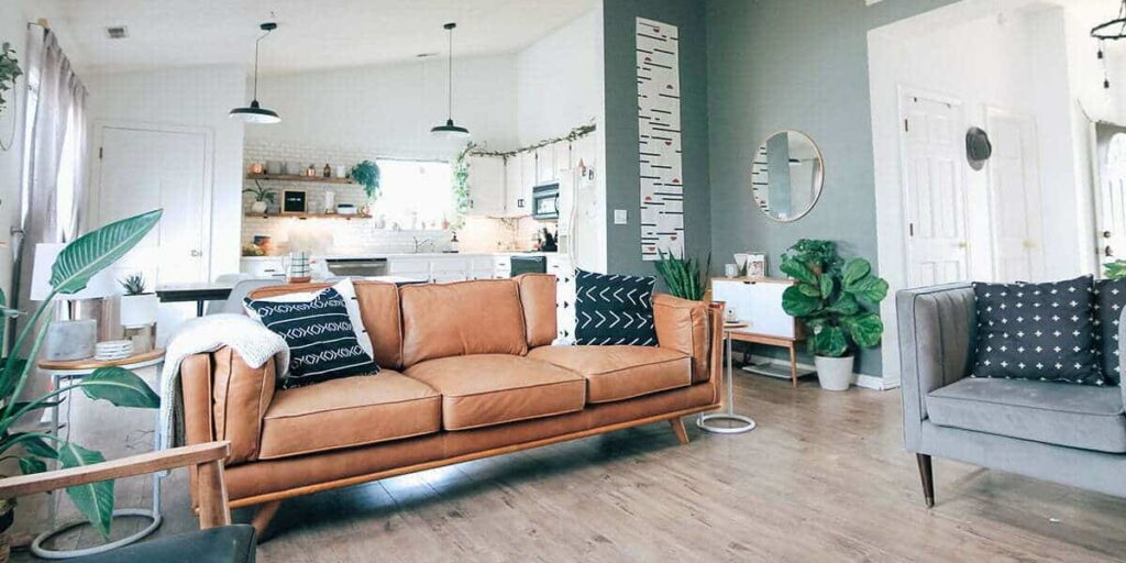 Bright open-plan living room with a tan leather sofa, patterned cushions and indoor plants