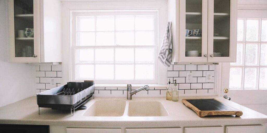 White subway tile kitchen splashback with dark grout lines behind a double sink and window